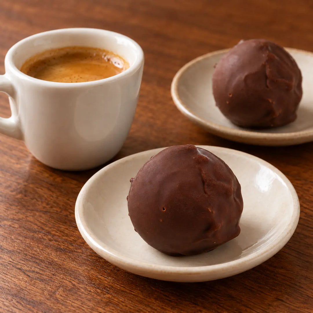 Schokoladen Trüffel auf kleinen Keramiktellern neben einem Espresso als Serviervorschlag.