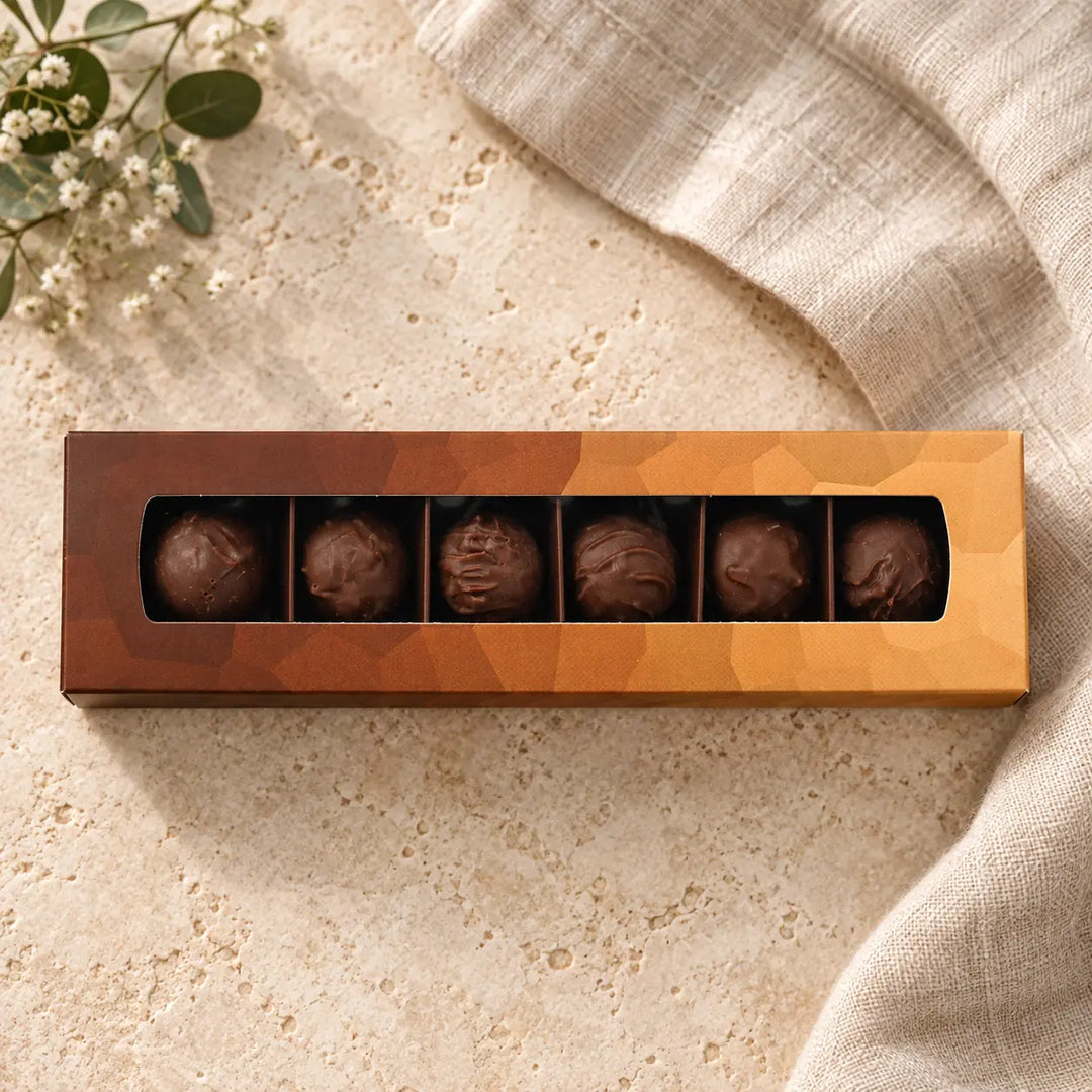 Schokoladen Trüffel in der originalen kupfer-orangefarbenen Box mit sechs Pralinen im langen Sichtfenster.