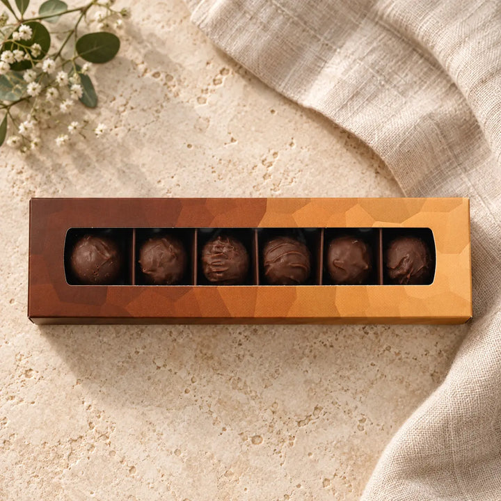 Schokoladen Trüffel in der originalen kupfer-orangefarbenen Box mit sechs Pralinen im langen Sichtfenster.