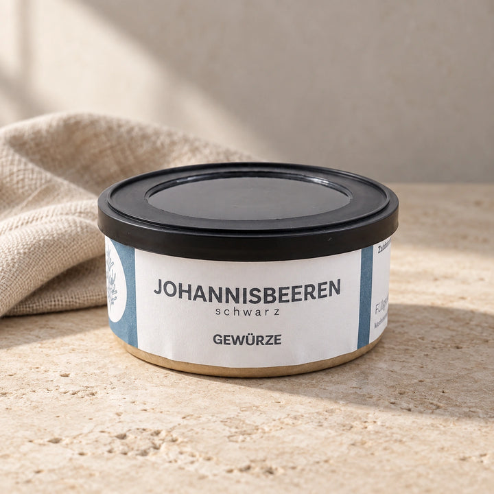 Originaldose Schwarze Johannisbeeren auf einer hellen Natursteinfläche neben einem Leinentuch.