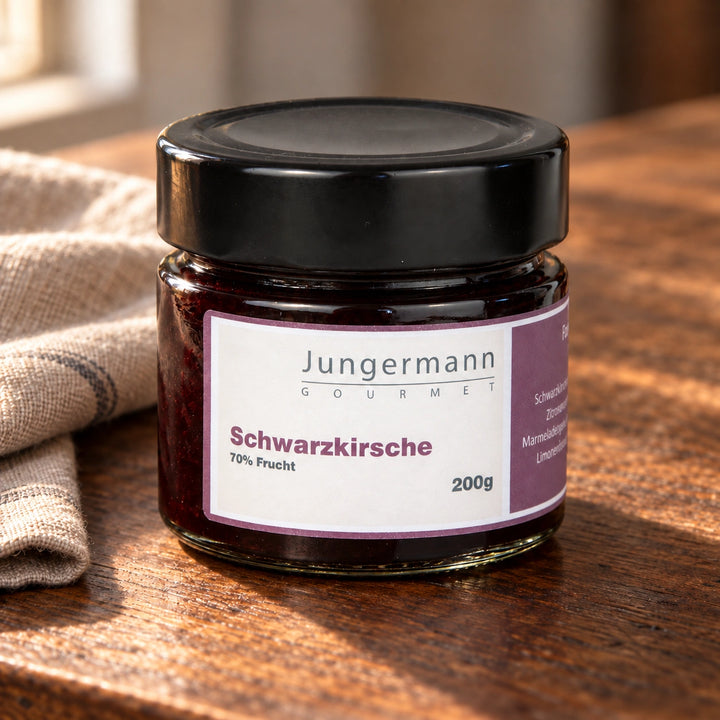 Schwarzkirschaufstrich im Originalglas auf dunklem Holz im warmen Seitenlicht.