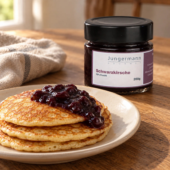 Pfannkuchen mit dunklem Schwarzkirschaufstrich neben dem Originalglas. Serviervorschlag.