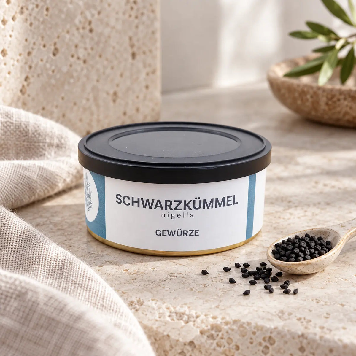 Schwarzkümmel in der originalen flachen Gewürzdose neben einem Löffel mit kleinen schwarzen Nigella-Samen.