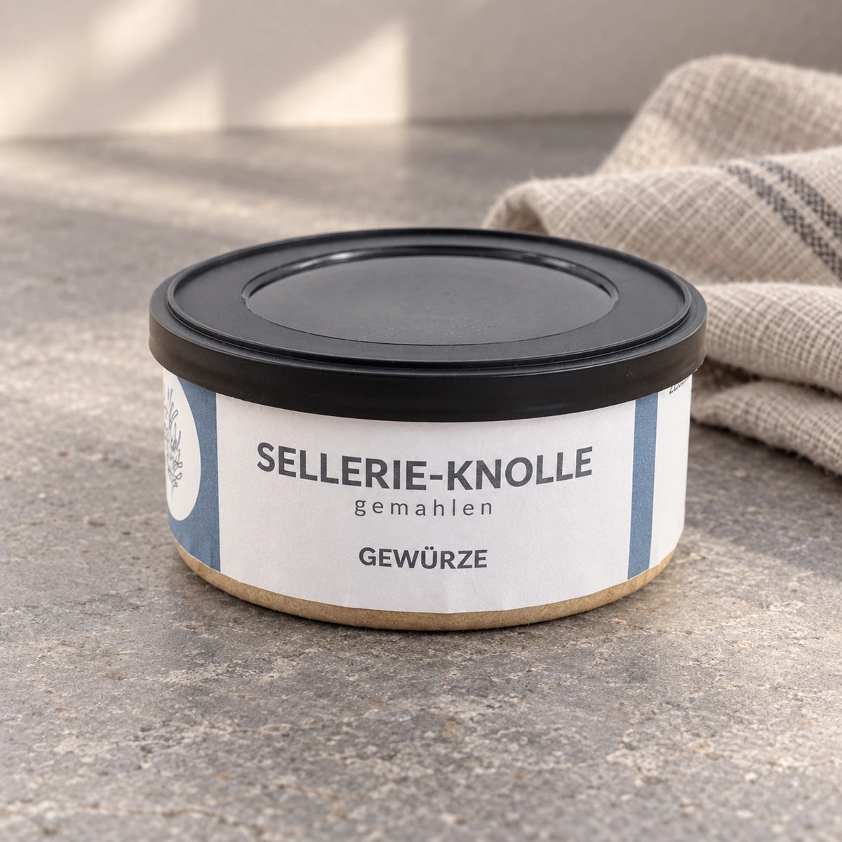 Originaldose Sellerie-Knolle gemahlen auf einer hellgrauen Arbeitsfläche neben einem Leinentuch.