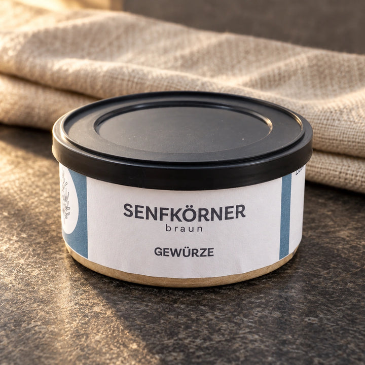 Originaldose Senfkörner braun auf einer dunklen Steinfläche neben einem Leinentuch.
