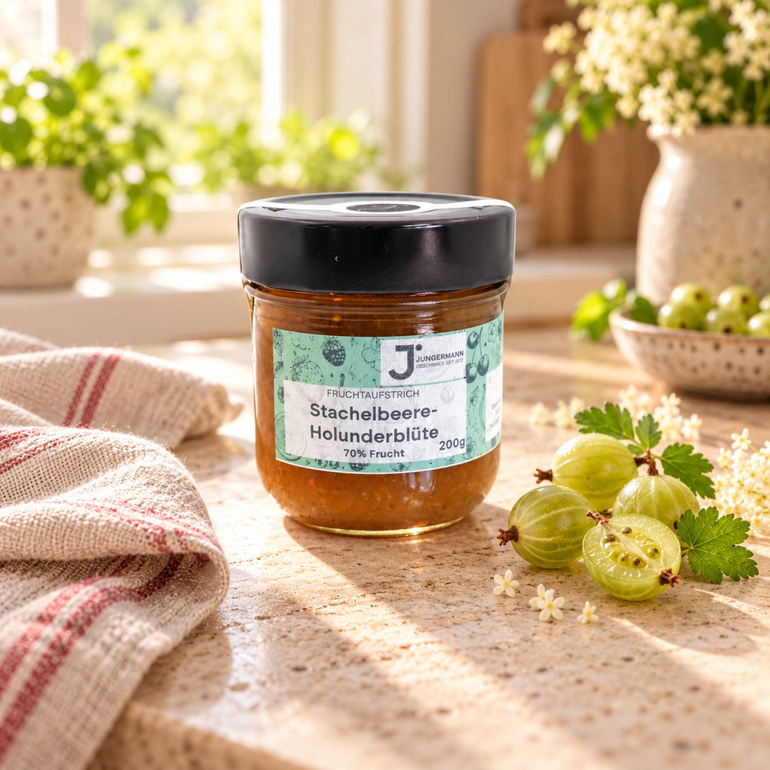 Stachelbeer-Holunderblüten Fruchtaufstrich von Jungermann Gourmet im 200-g-Glas auf hellem Naturstein mit grünen Stachelbeeren und Holunderblüten