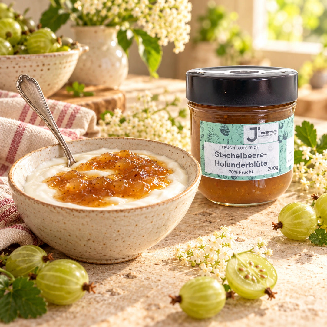 Serviervorschlag: Naturjoghurt mit Stachelbeer-Holunderblüten Fruchtaufstrich in einer Keramikschale neben dem Glas und grünen Stachelbeeren