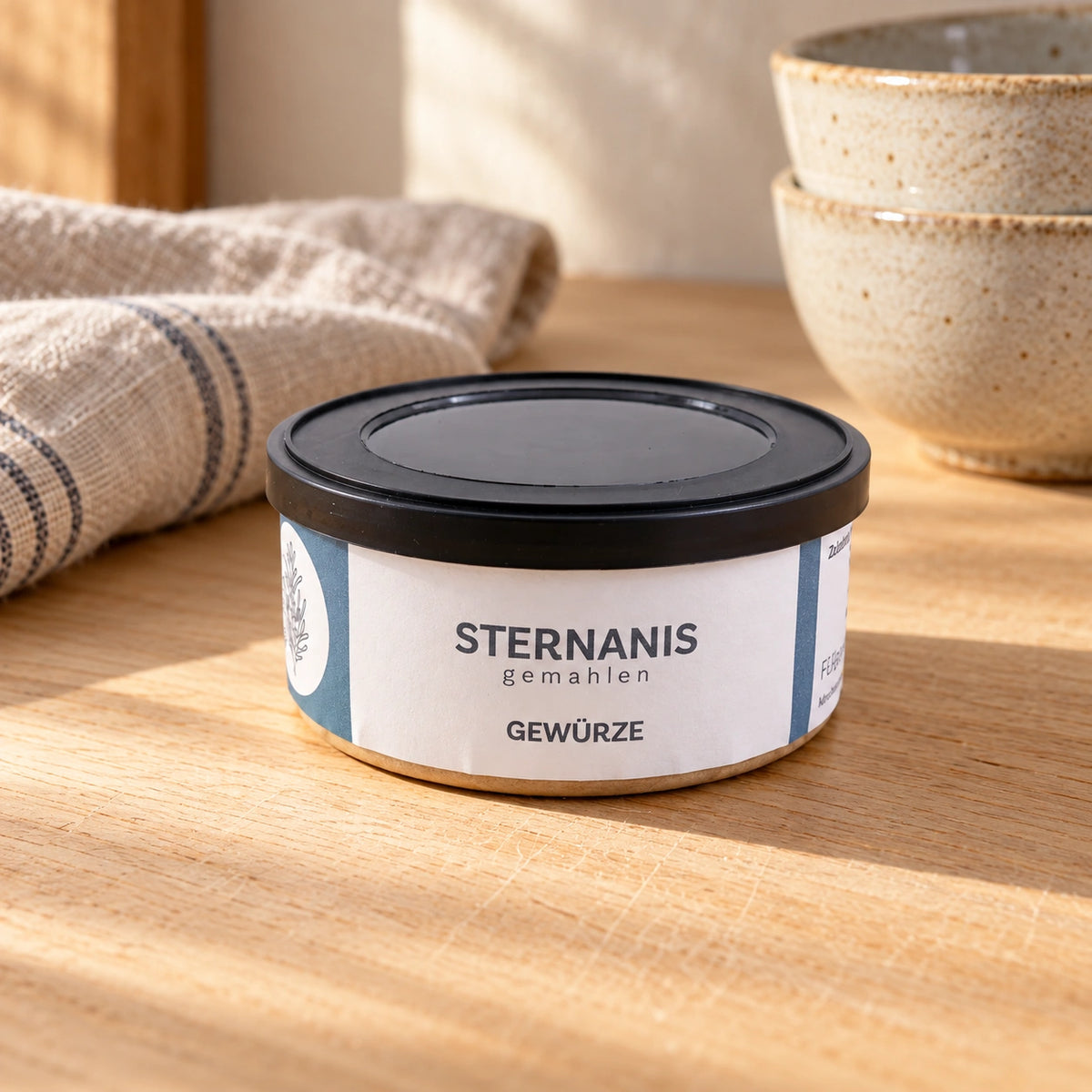 Originaldose Sternanis gemahlen auf einer hellen Backarbeitsfläche mit Leinentuch und Keramikschalen.