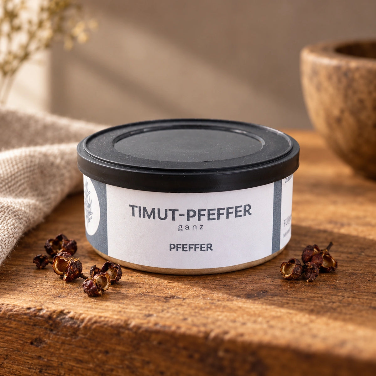 Timut Pfeffer in der Originaldose mit einigen rötlich-braunen Fruchtkapseln auf einem Holztisch.