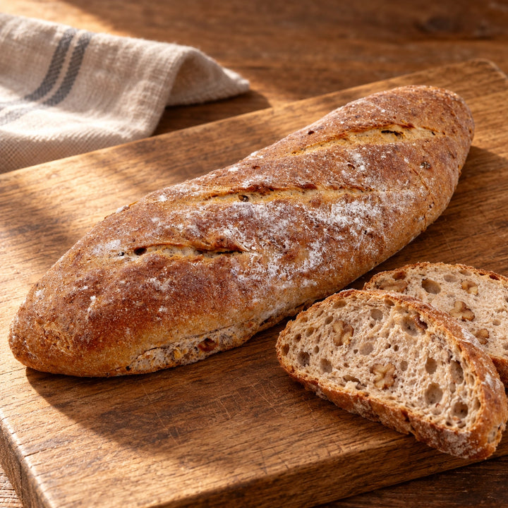 Walnuss-Baguette mit leicht bemehlter Kruste auf warmem Holz.
