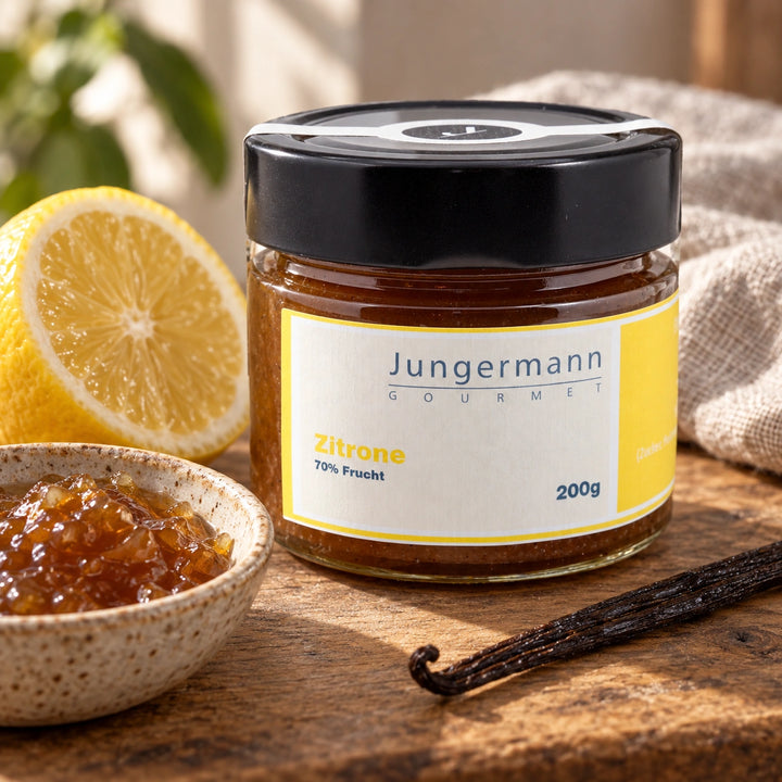Originalglas Zitronen-Aufstrich mit einer Zitronenhälfte, einer Vanilleschote und einer kleinen Schale Aufstrich.