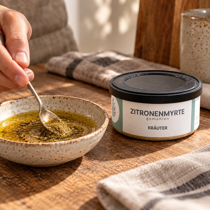 Eine Hand rührt gemahlene Zitronenmyrte in eine Ölmarinade; daneben steht die Originaldose. Zubereitungsvorschlag.